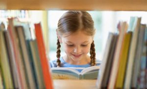 Nena llegint un llibre en una biblioteca per fomentar la lectura en infants